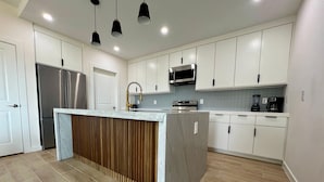 Una cocina moderna con armarios blancos, electrodomésticos de acero inoxidable y una isla central con panel de madera.