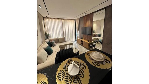 Ein modernes Wohnzimmer mit einer Couch, einem Esstisch mit Unterlagen und einem Fernseher im Hintergrund.