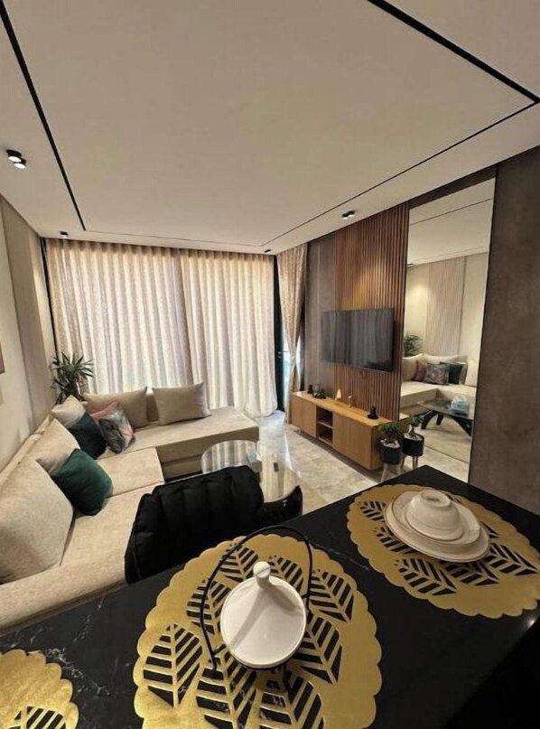 A modern living room with a sofa, a dining table with placemats, and a TV in the background.