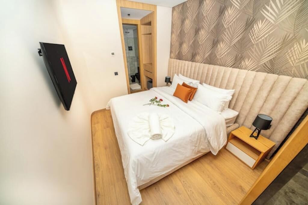 A neatly made bed with a white duvet, a wooden nightstand with a lamp, and a patterned wallpaper on the wall.