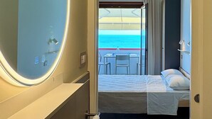 A hotel room with a bathroom featuring a sink and mirror, a bed with a view of the sea, and a balcony with a table and chairs. - Sulmare Studios - Molocali Sea View (Alba Adriatica)