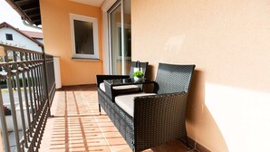 A balcony with a wicker chair, a small table with a plant, and a window. - Memory 04 - Double room (approx. 25 m²) with balcony on the 1st floor (Bischofsheim in der Rhön)