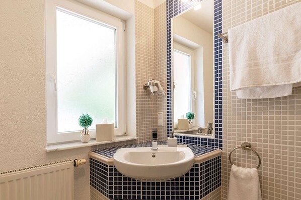 Ein Badezimmer mit weißem Waschbecken, einem Spiegel, einem Handtuchhalter und einem Fenster mit Jalousien.