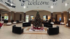 A lobby with a large 'Welcome' sign, a decorated Christmas tree, and Mickey Mouse murals. - Inspiration condo near Disney with free shuttle (Orlando)