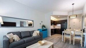 A modern living room with a grey sofa, a wooden coffee table, and a dining area with wooden chairs and a table. - Inspiration condo near Disney with free shuttle (Orlando)