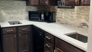 Une cuisine avec des meubles de rangement en bois foncé, un plan de travail blanc, un four à micro-ondes encastré et un lave-vaisselle.