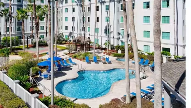 Un hôtel doté d’une piscine, de palmiers et d’un bâtiment blanc avec de nombreuses fenêtres.