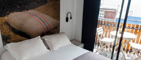 Un dormitorio moderno con una cama grande, un cabecero de diseño texturizado, un ventanal con vistas a la ciudad y una mesita de noche con una silla.