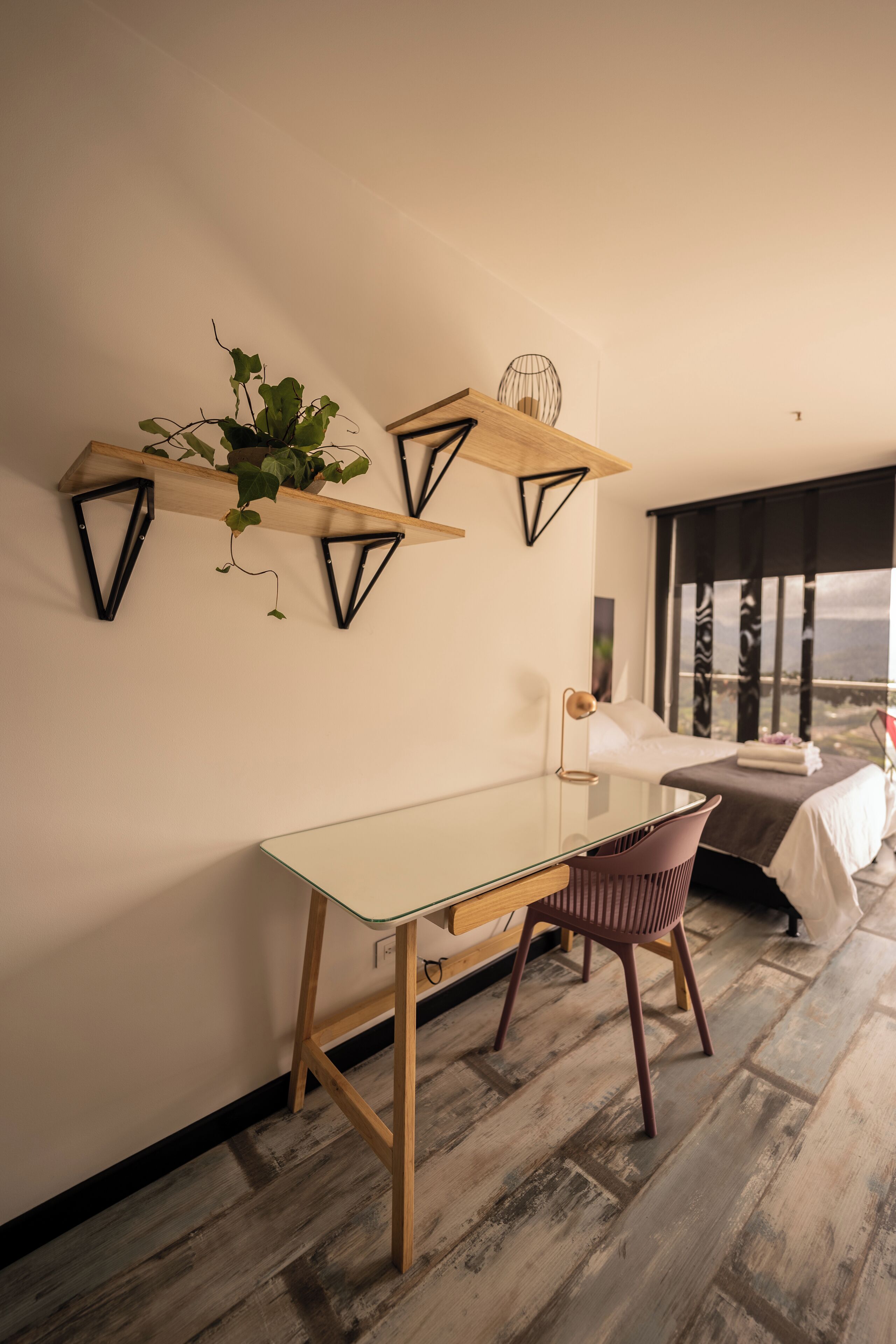 Una habitación moderna con una mesa de vidrio, piso de madera y una cama con vistas.