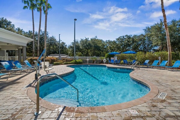 A swimming pool with blue water, surrounded by lounge chairs and palm trees.