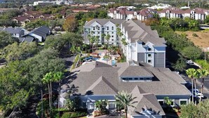 A large, multi-story hotel with a modern architectural design, featuring a central courtyard with palm trees and a swimming pool. - Condo near Disney-free shuttle to all theme parks (Orlando)