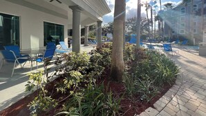A hotel courtyard with lounge chairs, a pool, and palm trees. - Condo near Disney-free shuttle to all theme parks (Orlando)