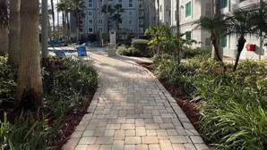 A pathway leading to a hotel with a pool, surrounded by palm trees and greenery. - Condo near Disney-free shuttle to all theme parks (Orlando)