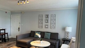 A living room with a sectional sofa, a round coffee table, a patterned rug, and decorative wall art. - Condo Near Disney-Universal-Epic-Sea World (Kissimmee)