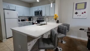 A modern kitchen with light blue cabinets, a white island with bar stools, a microwave, and a sink. - Amazing Condo near Disney World (Kissimmee)