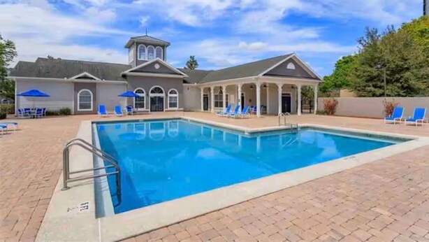 A swimming pool with a covered area, lounge chairs, and a building with a tower. - Amazing Condo near Disney World (Kissimmee)