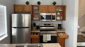 Una cocina compacta con armarios de madera, un refrigerador de acero inoxidable, un microondas, un horno y un lavamanos.