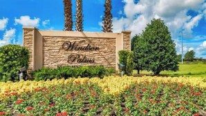 A sign for Windor Palms with a stone facade, palm trees, and a landscaped garden with various flowers.