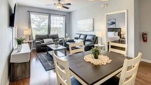 A modern living room with a dining table, sofas, and a ceiling fan.