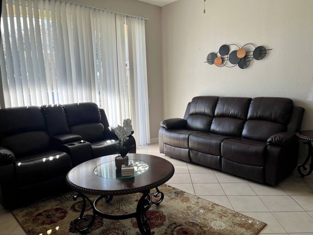 A living room with two black leather sofas, a glass coffee table, and a decorative wall piece.