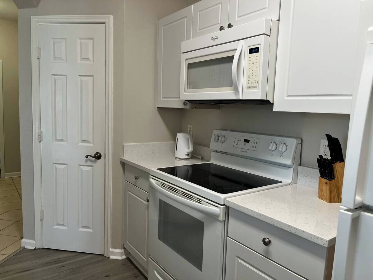 A compact kitchen with white cabinetry, a microwave, an oven, and a stovetop.