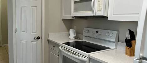 A compact kitchen with white cabinetry, a microwave, an oven, and a stovetop.