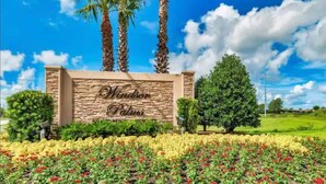 A sign for Windsor Palms with a stone wall, palm trees, and a field of flowers. - Apartment Disney Universal Epic (Kissimmee)