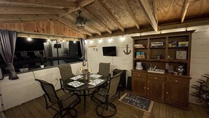 A wooden interior with a dining table, chairs, a cabinet, and a television. - Limestone Landing - Pool, firepit, covered patio, & more! (Kelleys Island)