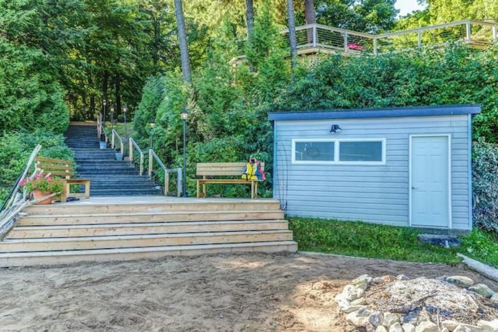 Un escalier en bois mène à un petit abri doté d’une porte et de fenêtres, entouré de verdure et agrémenté d’un foyer.