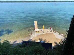 A clear view of a beach with a wooden pier extending into the water, a sandy area with a yellow umbrella, and a small structure with a flag.