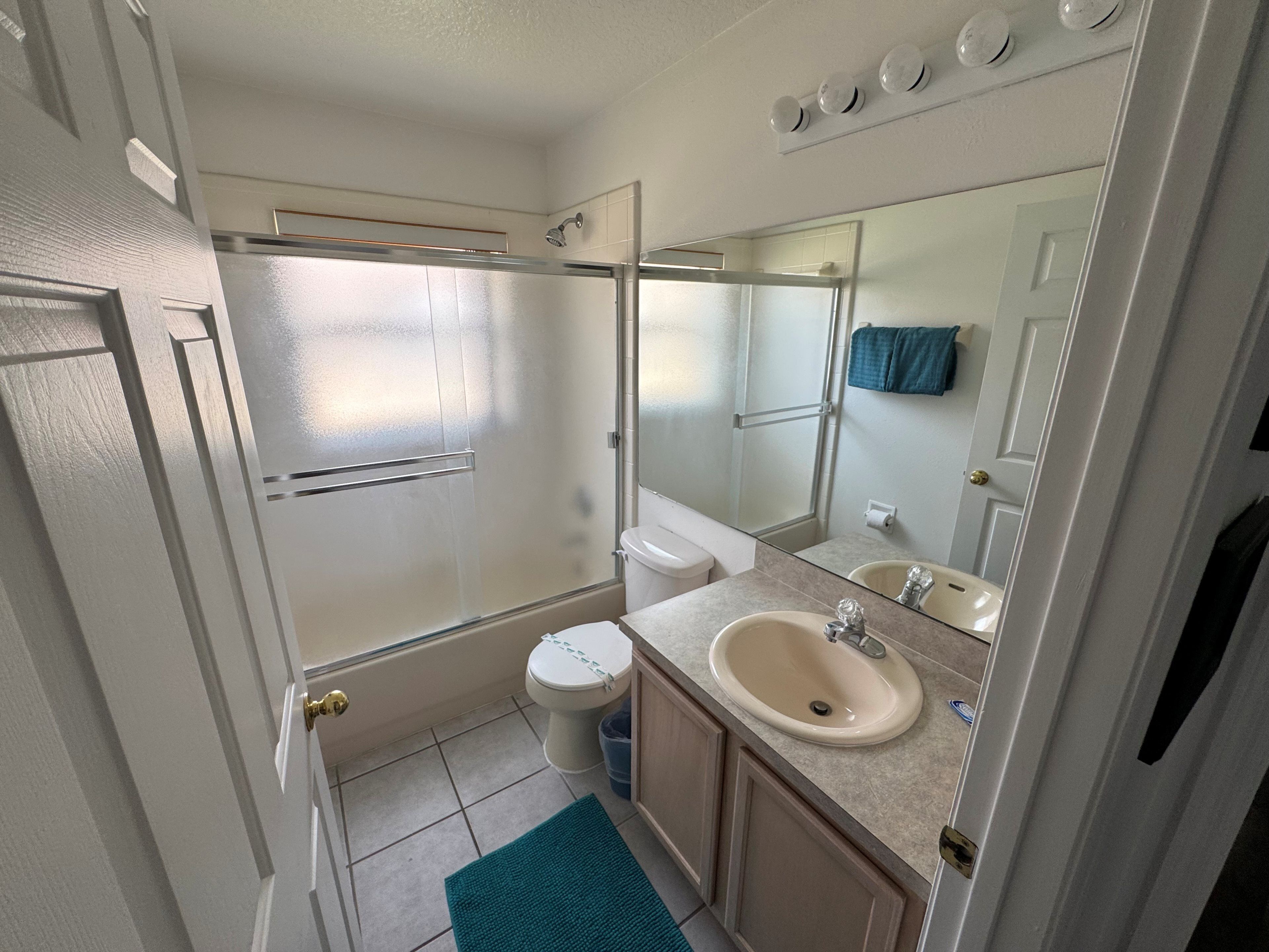 A bathroom with a shower, toilet, sink, and a mirror.