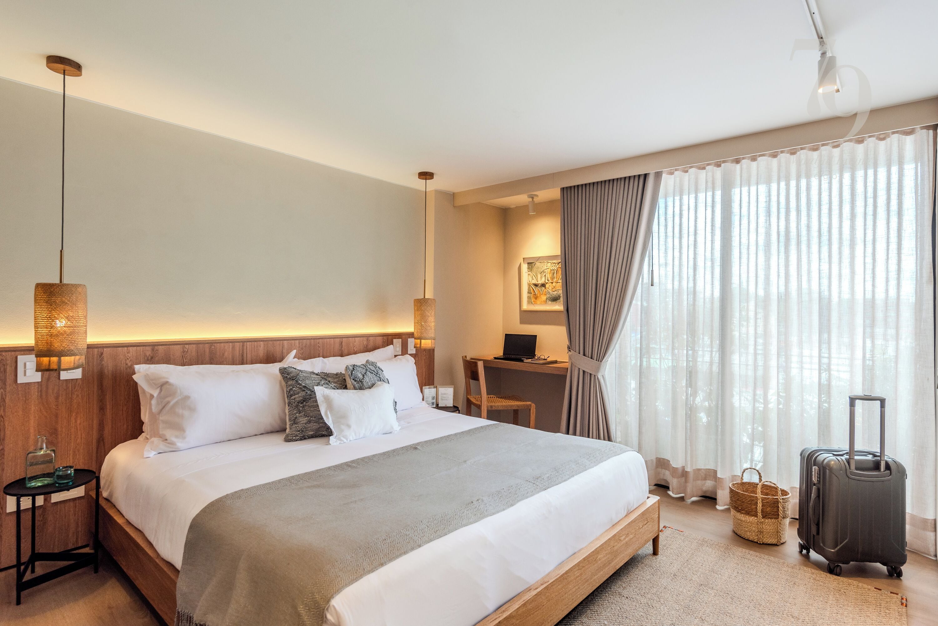 A hotel room with a large bed, a desk, a laptop, a suitcase, and a window with curtains.