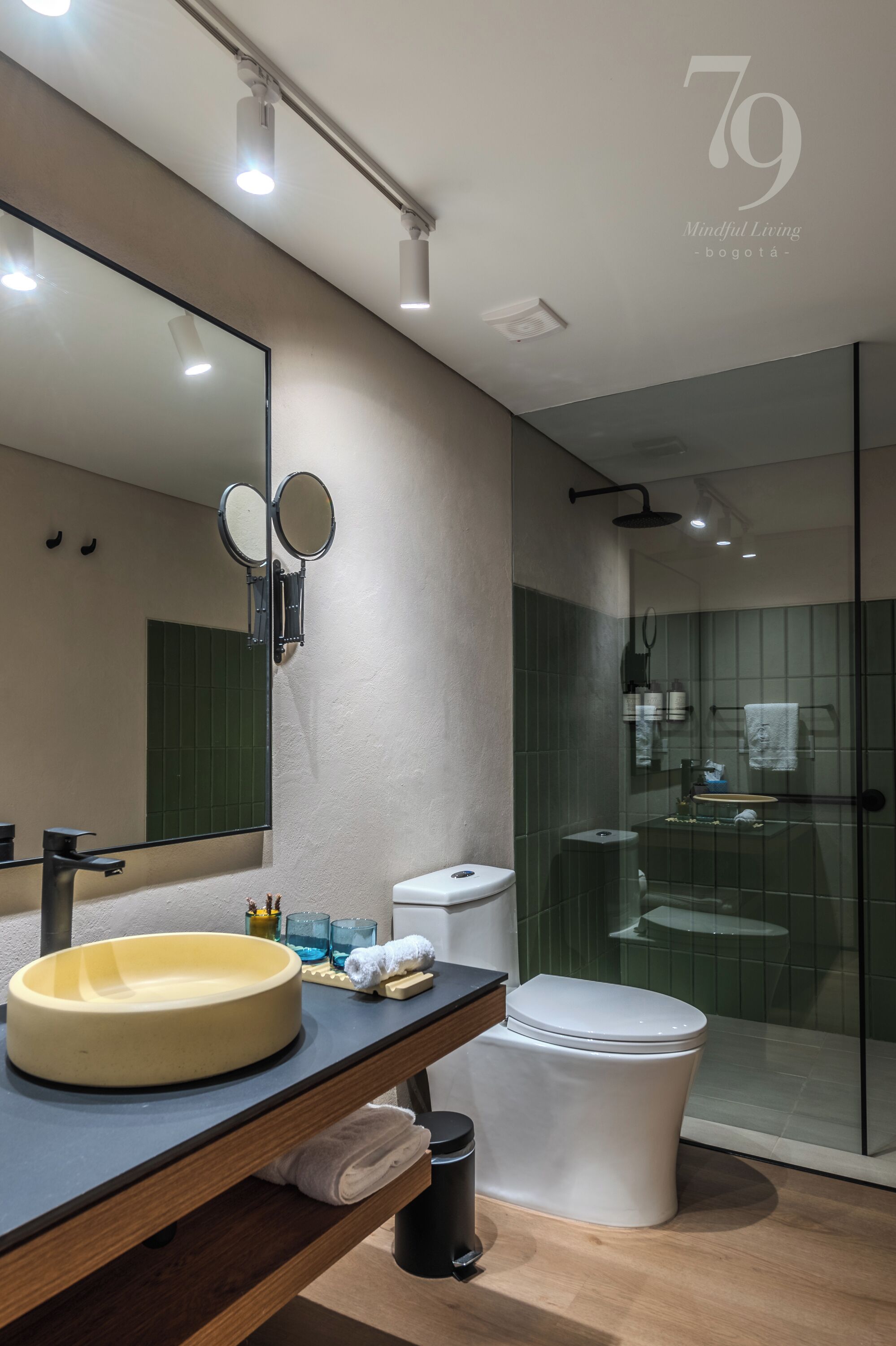 Une salle de bain moderne avec un grand miroir, un lavabo rond, des toilettes et une douche séparée par une paroi de verre.