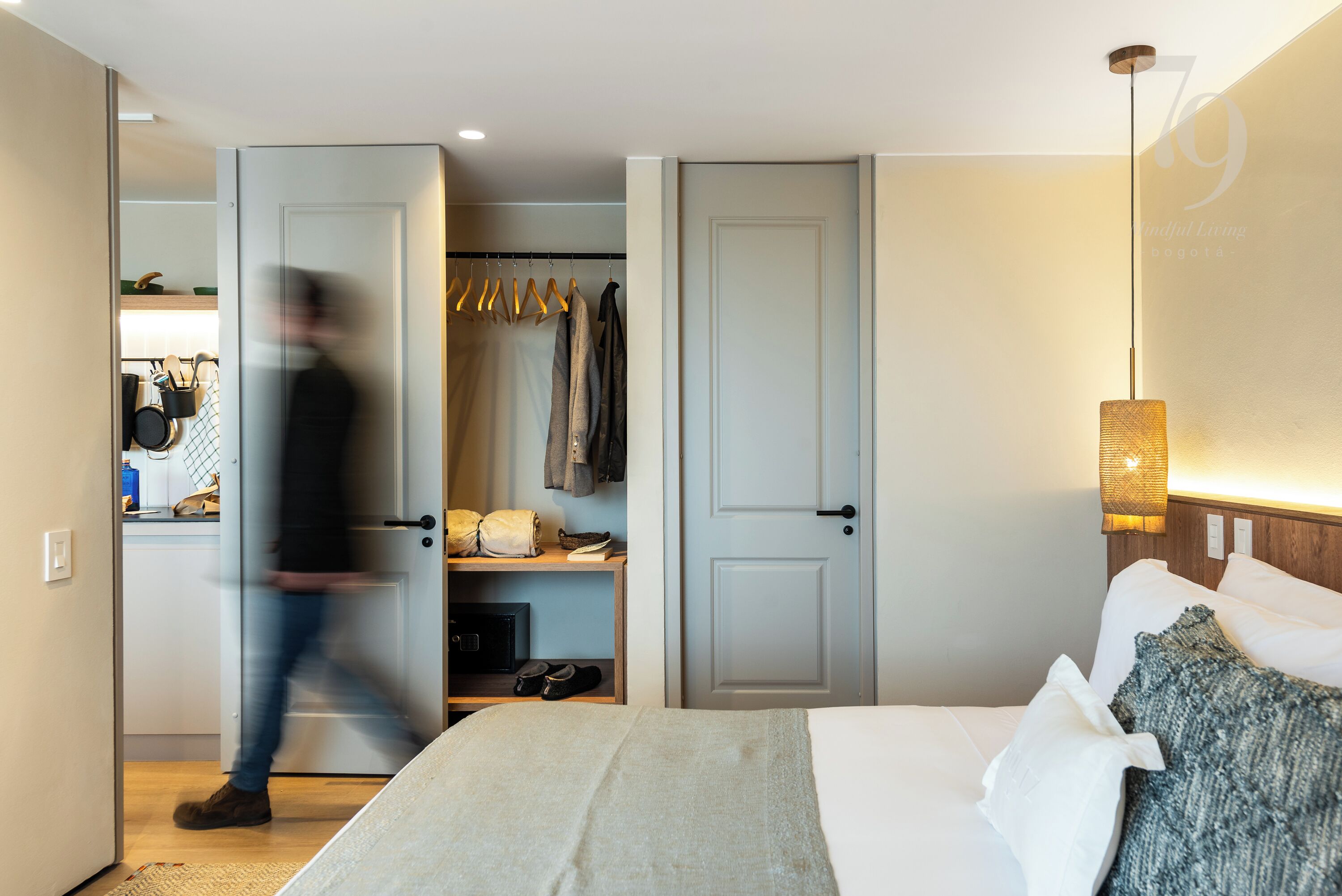A hotel room with a bed, a closet with hanging clothes, and a nightstand with a lamp.
