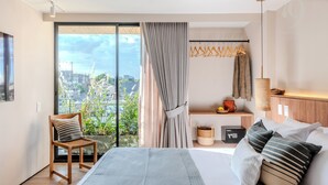 Un dormitorio moderno con una cama grande, una silla, una mesita de noche, una lámpara colgante y vistas a la ciudad a través de un ventanal amplio.