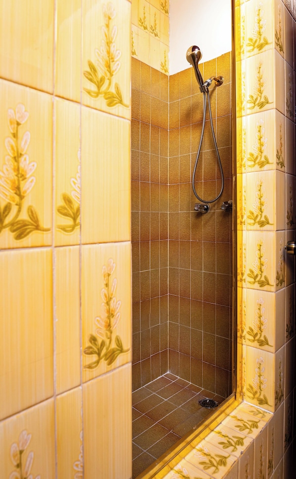 A shower with a handheld showerhead, tiled walls with floral patterns, and a drain at the bottom.