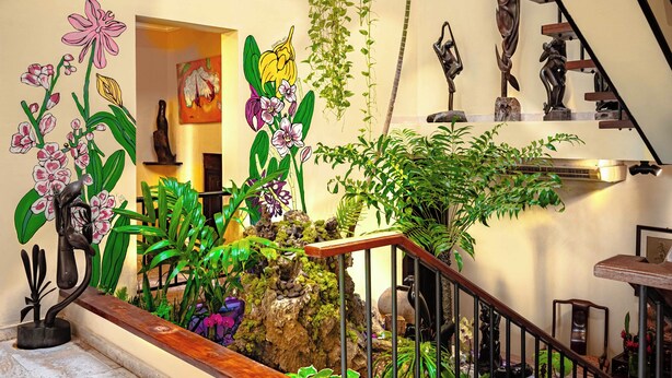 A staircase with a wooden handrail, surrounded by various plants and sculptures. - Casa Orquídea (Panama City)