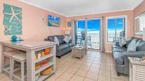 A cozy living room with a grey sofa, a coffee table, and a TV. There's a balcony with a view of the beach. - Oceanfront Gem (Myrtle Beach)
