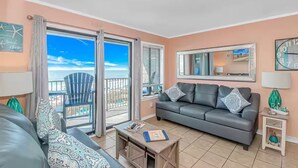 A living room with a grey sofa, a coffee table, and a balcony with a view of the beach. - Oceanfront Gem (Myrtle Beach)