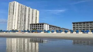A beachfront hotel with multiple buildings, a sandy beach, and umbrellas. - Oceanfront Gem (Myrtle Beach)