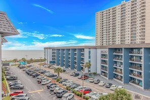A multi-story parking garage with a row of cars parked in front of a building with balconies.