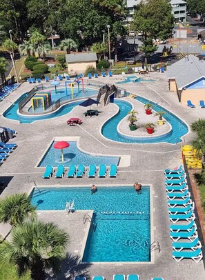 A swimming pool area with multiple pools, lounge chairs, and palm trees.