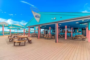 A deck with picnic tables and umbrellas, a bar area, and a sign reading "The Quarter Deck".