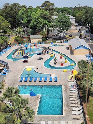 A large outdoor swimming pool with multiple lanes, surrounded by lounge chairs and umbrellas.