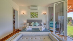 A bedroom with a large bed, two bedside lamps, a wall-mounted air conditioner, and a view of the outdoors. - Villa Kentia Mallorca, stylish country house close to Palma (Palma)