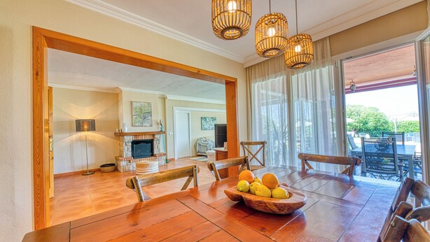 A spacious dining area with a wooden table, chairs, and a fruit bowl. There is a fireplace, a television, and a view of the outdoors through large windows. - Villa Kentia Mallorca, stylish country house close to Palma (Palma)