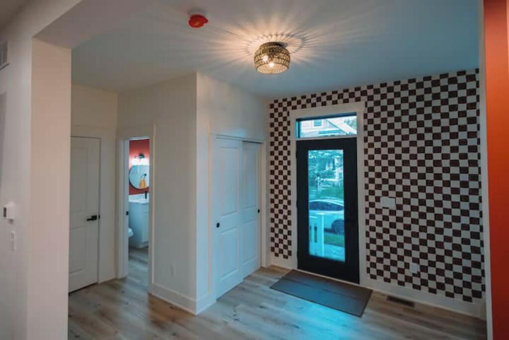 A hallway with a checkered wall pattern, a door leading to a bathroom, and a ceiling light fixture.