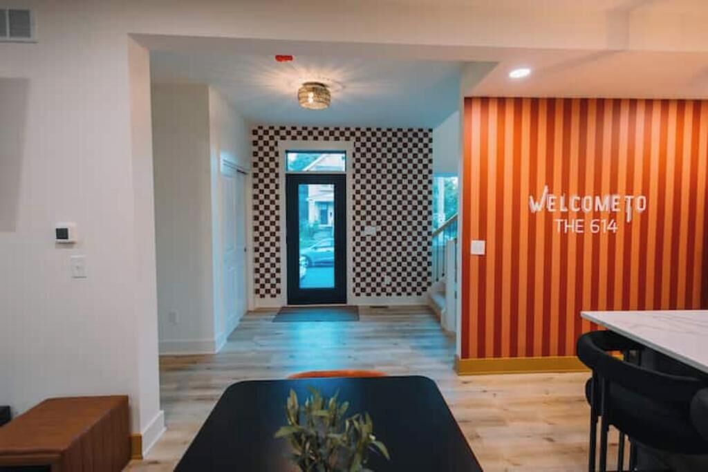 A modern hotel lobby with a checkered wall pattern, a 'Welcome to The 614' sign, and a dining area with a black table and chairs.