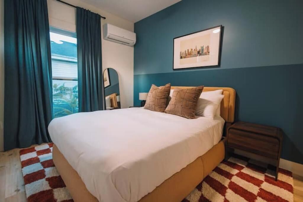 A bedroom with a large bed, a cityscape picture on the wall, and a window with curtains.