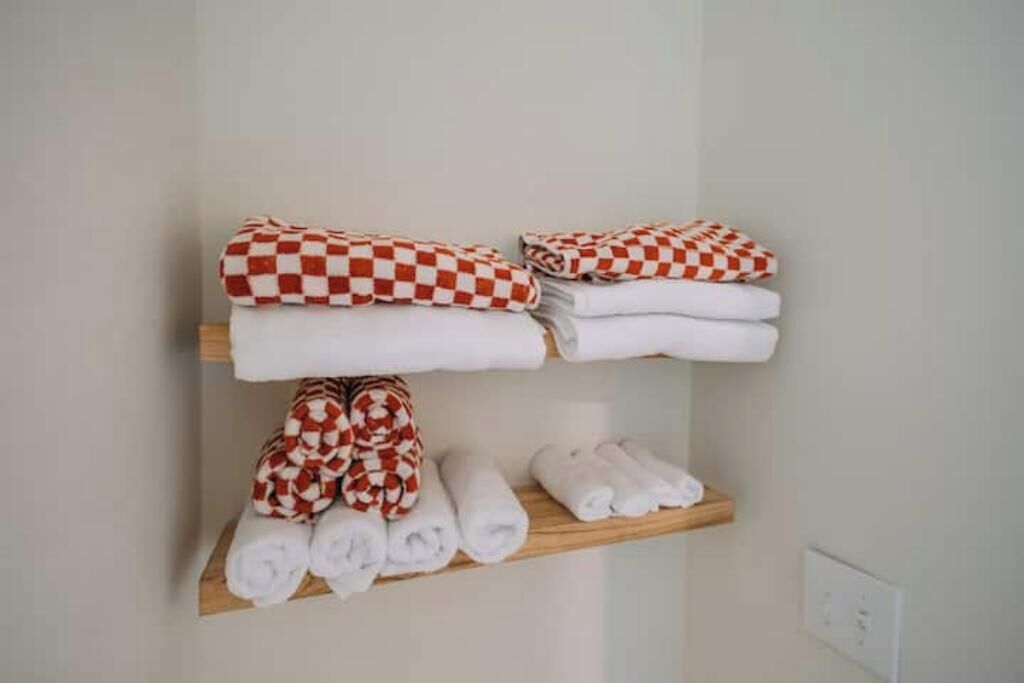 Une chambre d’hôtel avec une étagère en bois où sont soigneusement pliées des serviettes aux motifs écossais rouges et blancs, ainsi que des serviettes blanches unies.